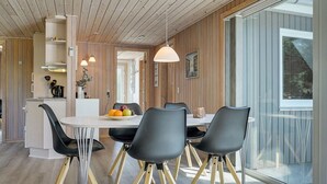Een moderne eetruimte met een witte tafel, zwarte stoelen met houten poten en een groot raam.