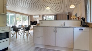 Een moderne keuken met houten kasten, een eethoek met stoelen en een groot raam dat natuurlijk licht binnenlaat.