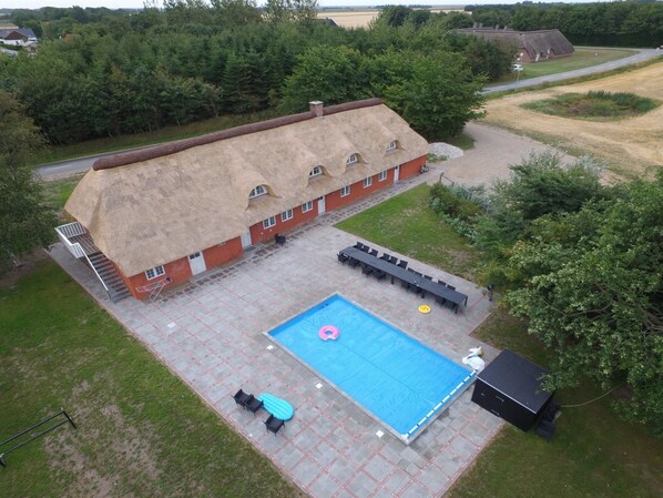 Un edificio con tetto di paglia, una piscina, posti a sedere all'aperto e un piccolo deposito.