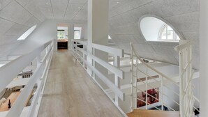 Een ruim interieur met hoge plafonds, een centrale trap en grote ramen voor natuurlijk licht.