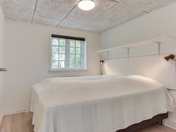 A bedroom with a large bed, a window with blinds, a ceiling light, and a wall-mounted lamp.
