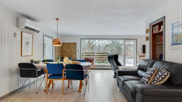 Ett modernt vardagsrum med en matplats, med en svart lädersoffa, blå stolar och ett matbord i trä.