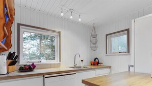 Ett kök med vita skåp, en träbänkskiva, en diskmaskin och ett fönster med utsikt över träd.