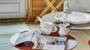 A wooden interior with a table set for breakfast, including a newspaper, a mug, a pitcher, and a plate with a pastry.