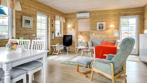 A cozy cabin interior with a dining area, a living room with a sofa and armchair, and a television.