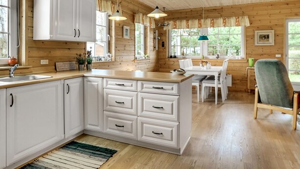 A cozy cabin-style kitchen with white cabinetry, a wooden countertop, and a dining area with a table and chairs.