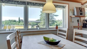 A dining area with a table, chairs, a hanging light fixture, and large windows with a view of trees and buildings.