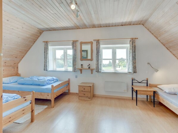 A cozy attic bedroom with two wooden beds, a small wooden table, and a radiator.