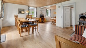 Amplia sala de estar con techo de madera, una mesa de comedor con sillas, un sofá, un televisor y una chimenea.