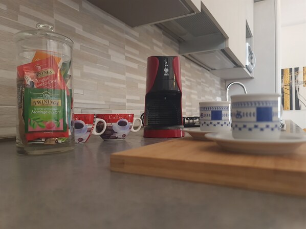 A kitchen counter with a coffee maker, two coffee cups, a glass jar of tea, and a ceramic mug. - *4 double bedrooms *fully equipped kitchen *2 living rooms with smart TVs *air conditioning (L'Aquila)