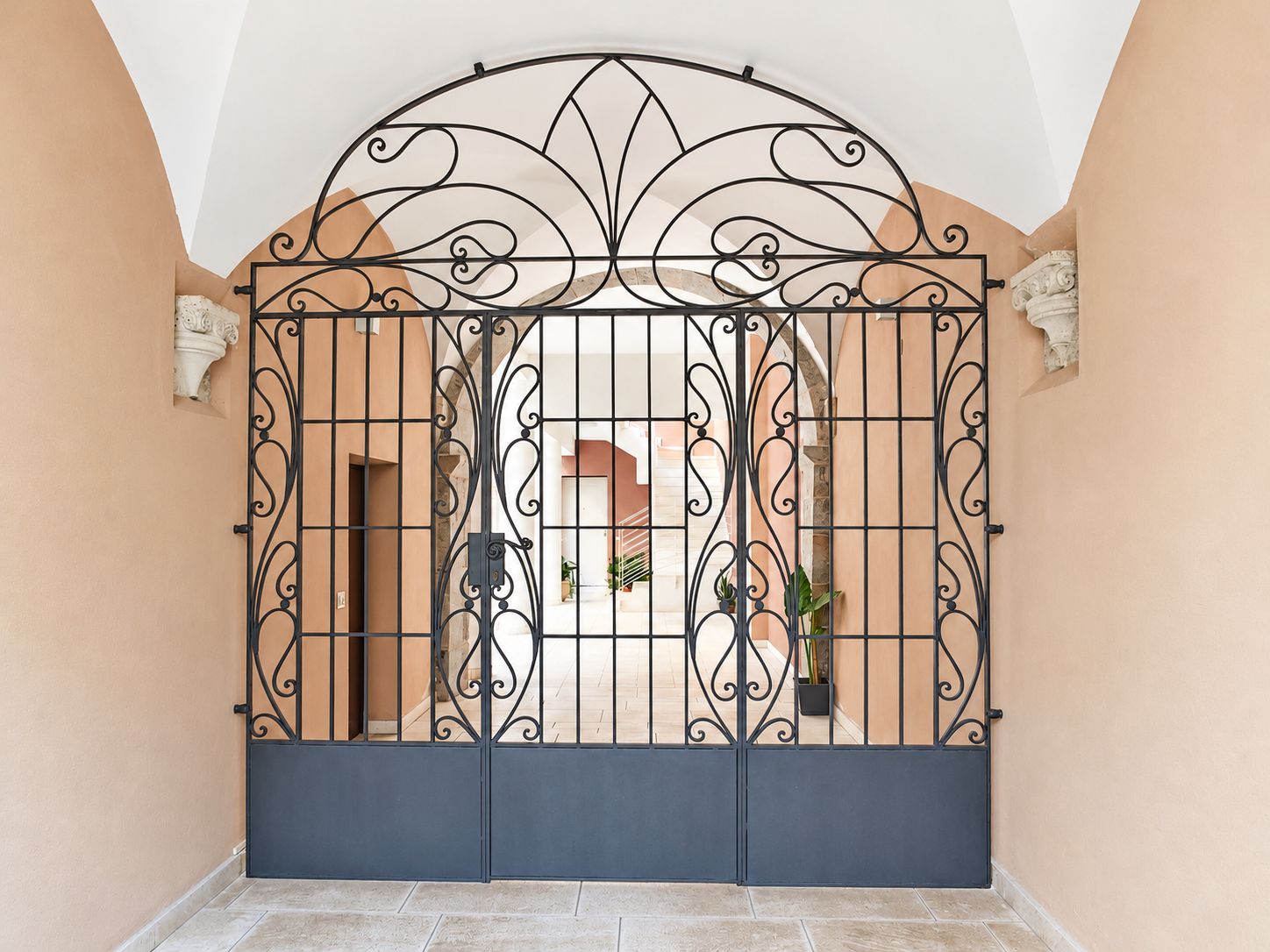 A gated entrance with a decorative metal gate, a tiled floor, and a beige wall.