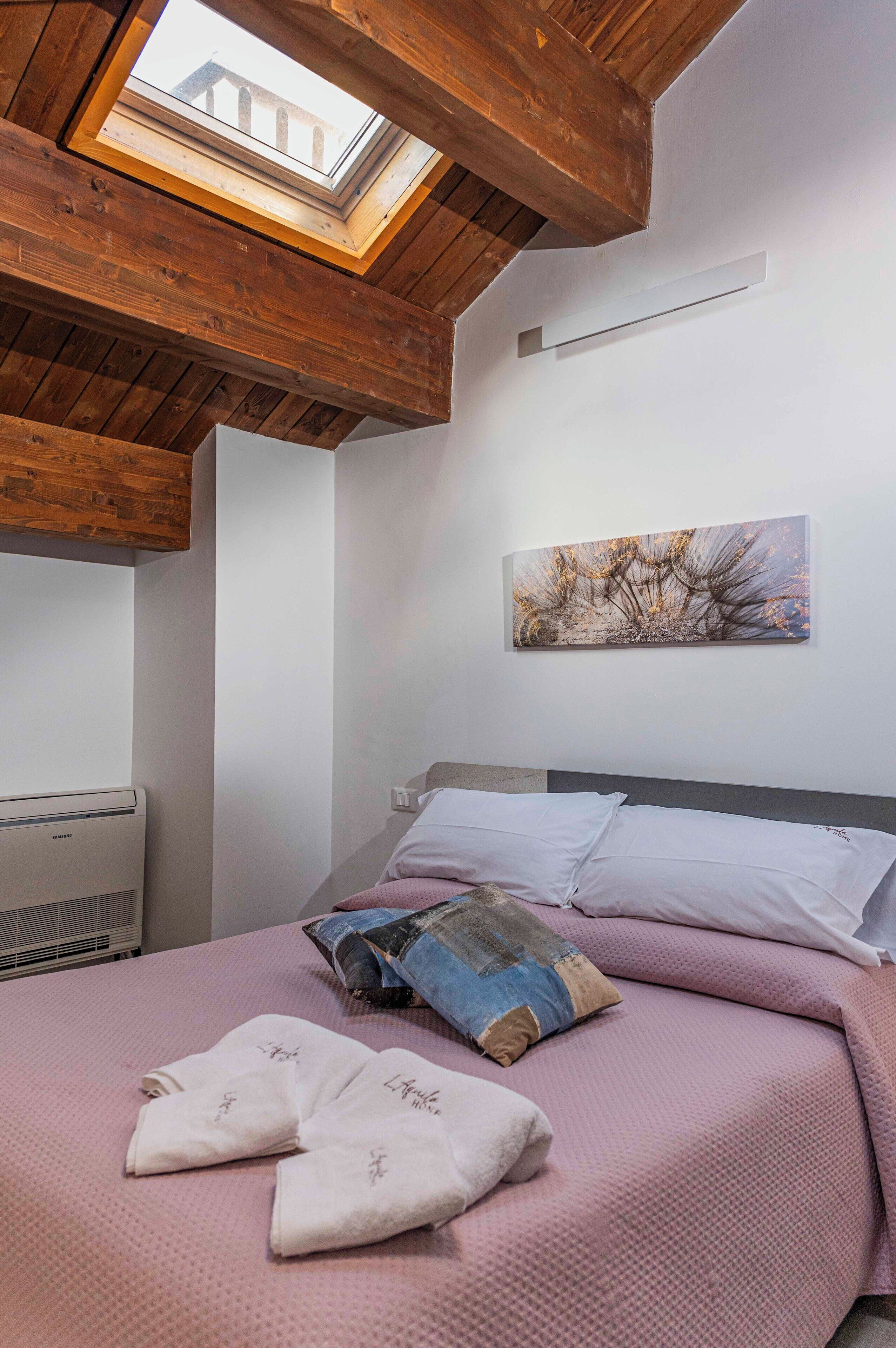 Une chambre avec une lucarne, un lit avec une literie rose, un tableau au mur et un radiateur.