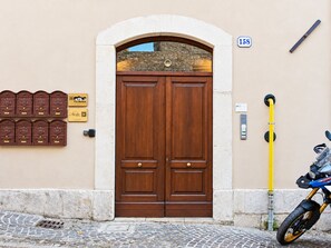 A double wooden door with a stone archway, a mailbox with a crest, a yellow pole, and a motorcycle. - *4 double bedrooms *fully equipped kitchen *2 living rooms with smart TVs *air conditioning (L'Aquila)