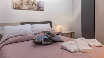 Un lit bien fait, avec une couvre-lit rose, deux oreillers et trois serviettes pliées, chacune portant une inscription.