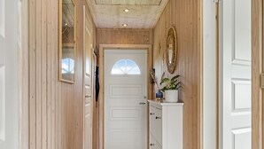Un couloir aux murs en bois, une porte blanche et une petite armoire contenant des objets décoratifs.