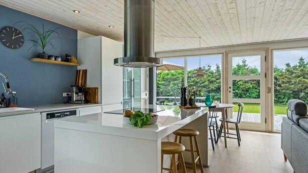 Une cuisine moderne dotée d’un îlot central, d’un plafond en bois et offrant une vue sur le jardin grâce à de grandes portes coulissantes.