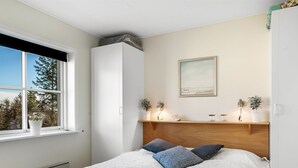 A bedroom with a bed, a window, a wardrobe, a shelf with decorative items, and a framed picture on the wall. - "Dafna" - 100m from the sea by Interhome (Hals)