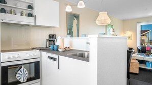 A compact kitchen with a stove, oven, and dishwasher, a small island with a sink, and pendant lighting. - "Dafna" - 100m from the sea by Interhome (Hals)