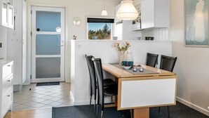 A modern kitchen with a dining area, featuring a wooden table, black chairs, and a window with a view of trees. - "Dafna" - 100m from the sea by Interhome (Hals)