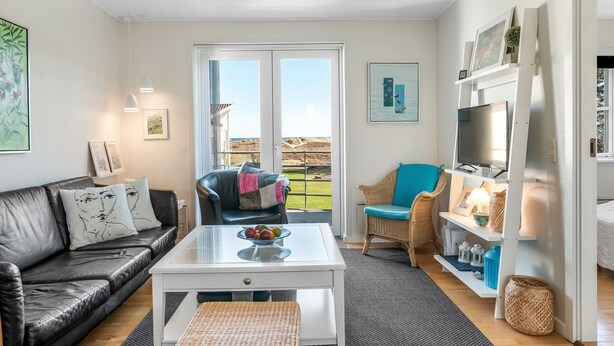 A modern living room with a leather sofa, a glass coffee table, a wicker ottoman, and a television on a white stand. - "Dafna" - 100m from the sea by Interhome (Hals)