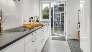 A modern kitchen with a large island, white cabinetry, and a sliding glass door leading to a patio. - "Hejdie" - 150m from the sea by Interhome (Hals)