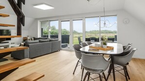 A modern living space with a dining area, a grey sofa, wooden beams, and large windows offering a view of the outdoors. - "Hejdie" - 150m from the sea by Interhome (Hals)