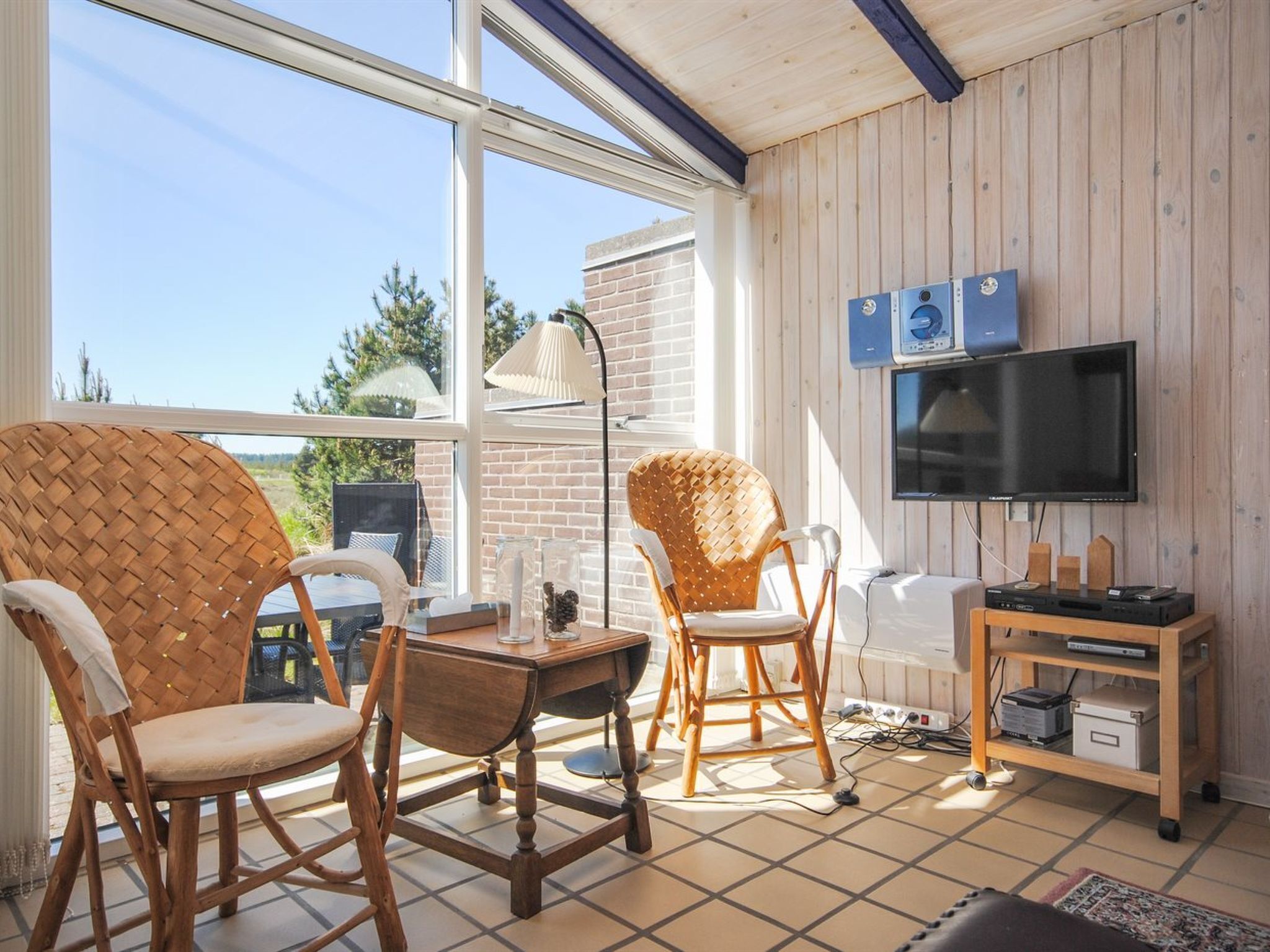Een gezellige kamer met rieten stoelen, een houten tafel, een televisie en een klein plankje met elektronische apparaten.