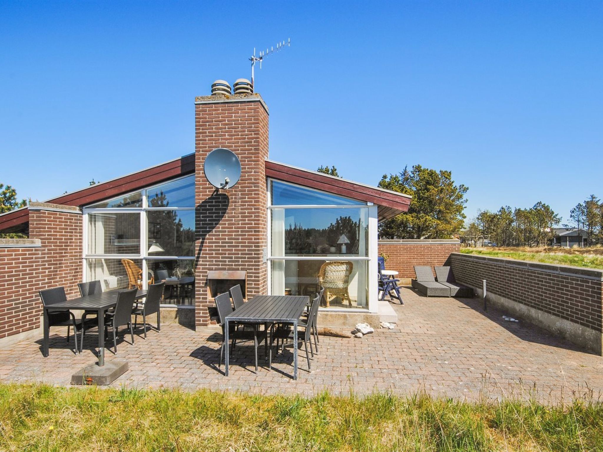 Una casa moderna con fachada de ladrillo, grandes ventanales y un patio con mobiliario exterior.