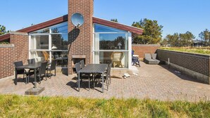 Ein modernes Haus mit Backsteinfassade, großen Glasfenstern und einer Terrasse mit Gartenmöbeln.