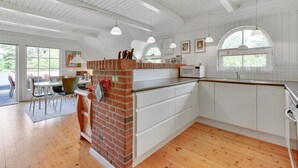 Una cocina moderna con muebles blancos, una pared de ladrillo decorativa y un área de comedor con una mesa y sillas.