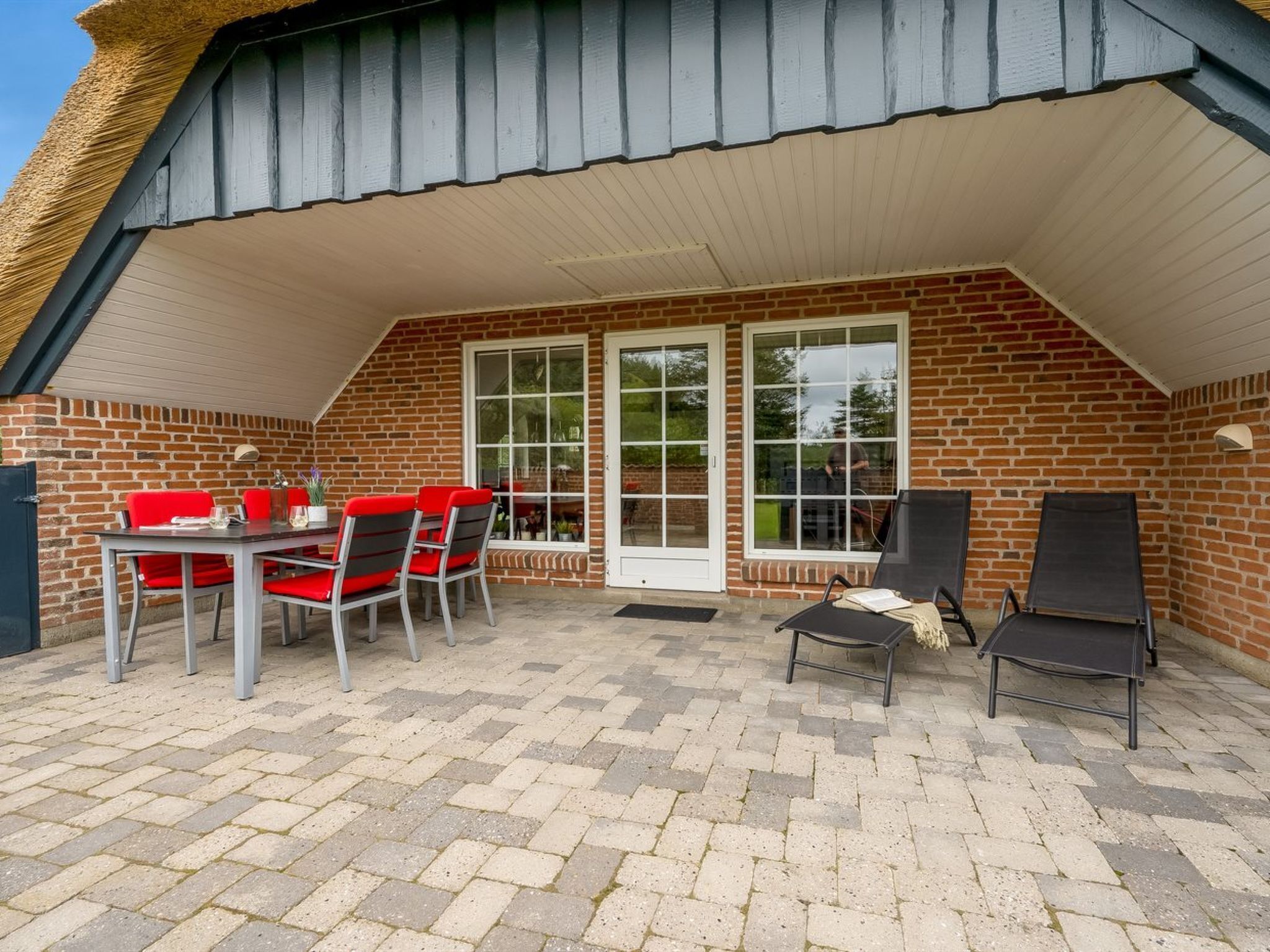 A patio with a brick wall, a table with red chairs, and two black lounge chairs.