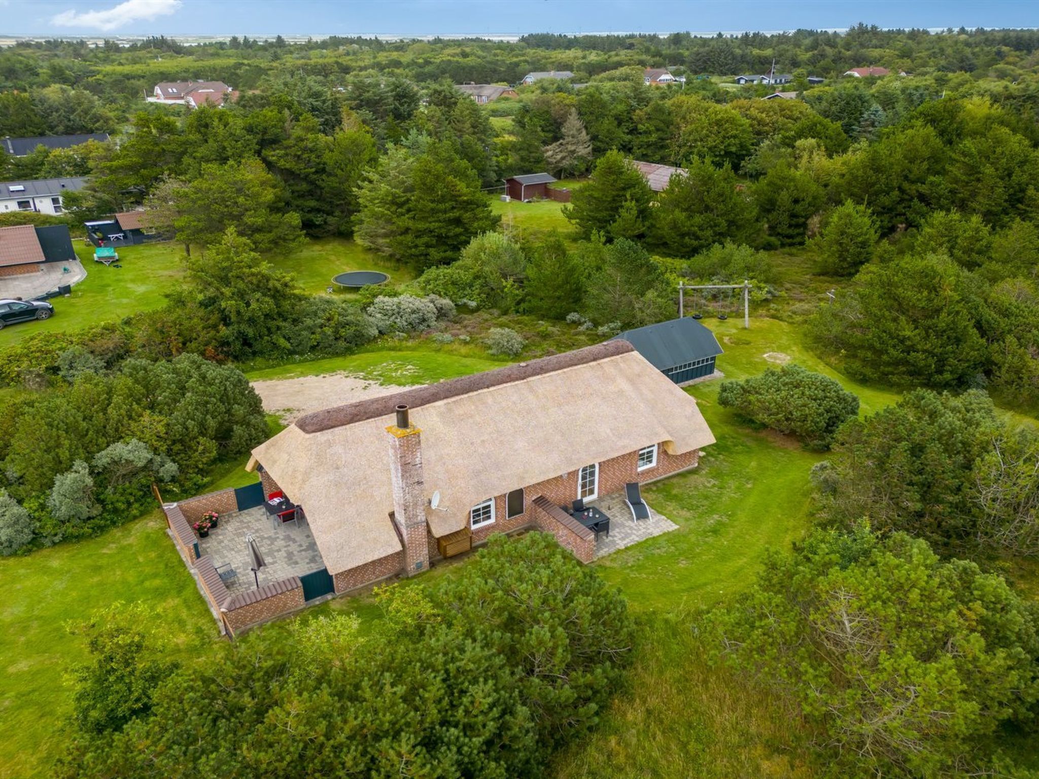 A single-story house with a thatched roof, surrounded by a well-maintained lawn and dense trees.