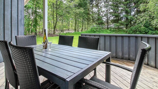 A covered outdoor dining area with a table and chairs, surrounded by a wooden deck and a view of a forested area. - "Frederikke" - 28km from the sea by Interhome (Toftlund)