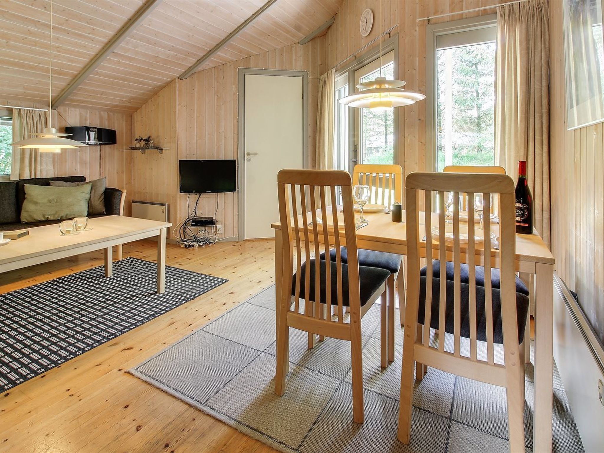 A cozy cabin interior with a dining area, a sofa, and a television.