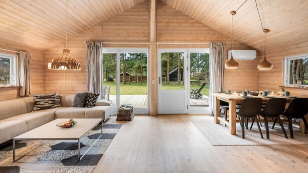 A spacious cabin interior with a dining area, sofa, and large windows.