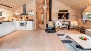 A modern log cabin interior with a kitchen, dining area, and a wood-burning stove.