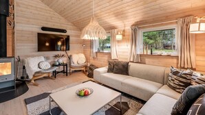 A cozy cabin interior with a wooden ceiling, a sofa, a coffee table, a fireplace, and a window with curtains.