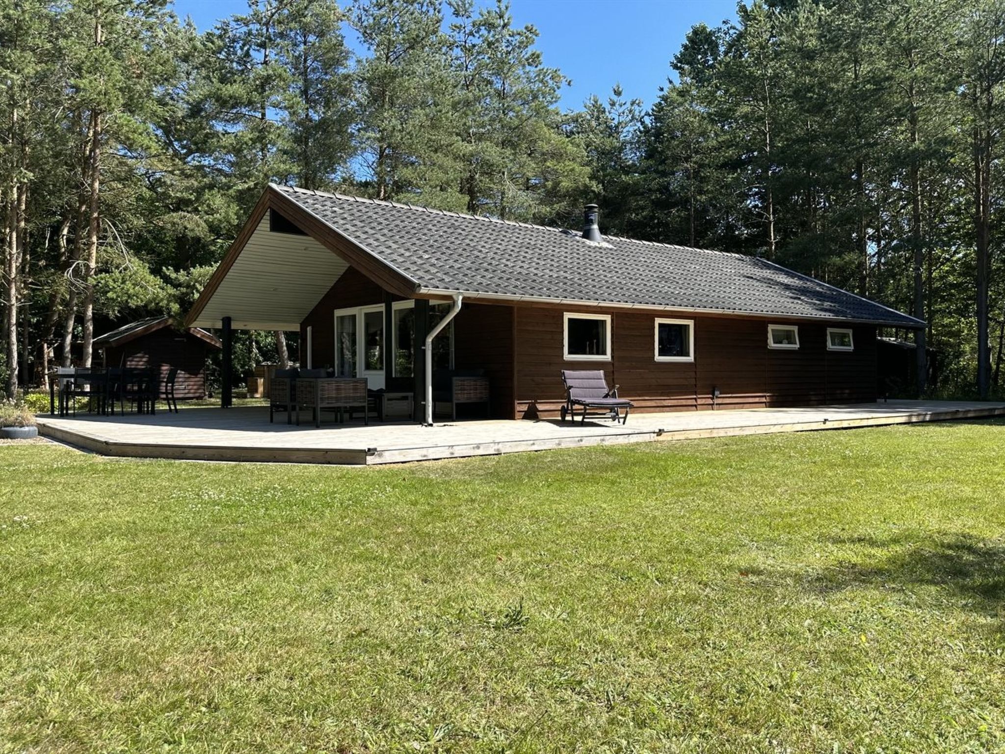 Een gelijkvloers vakantiehuisje met een overdekt terras, een klein dek en een gazon.