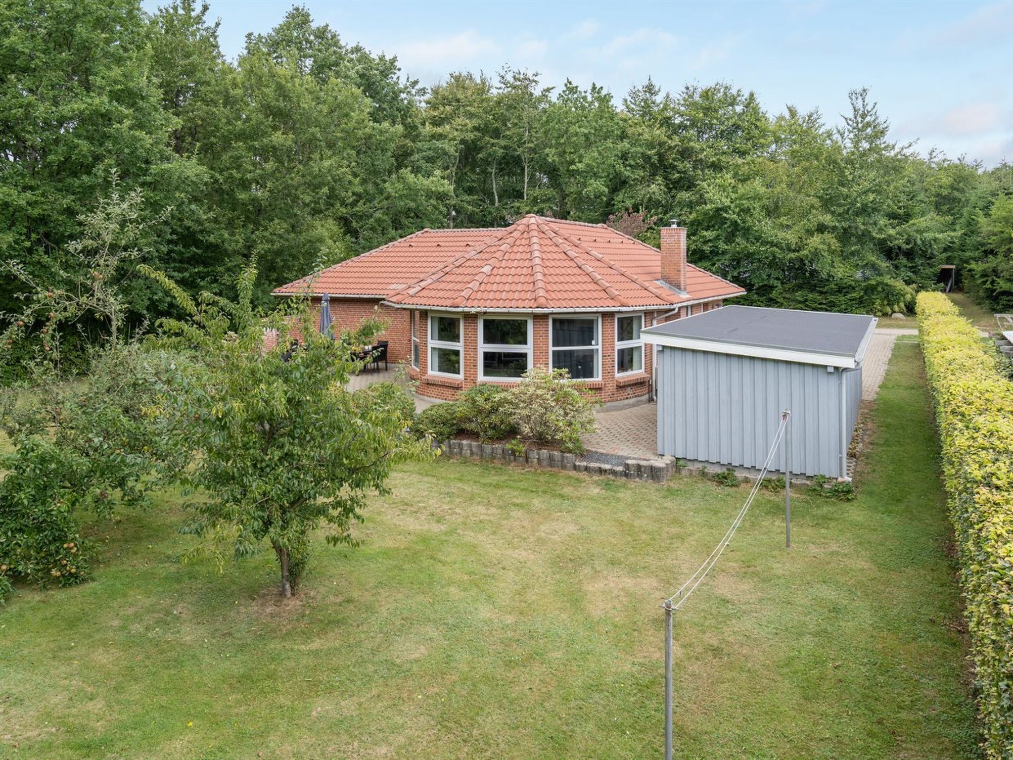 A single-story house with a red-tiled roof, a brick exterior, and a small attached shed.