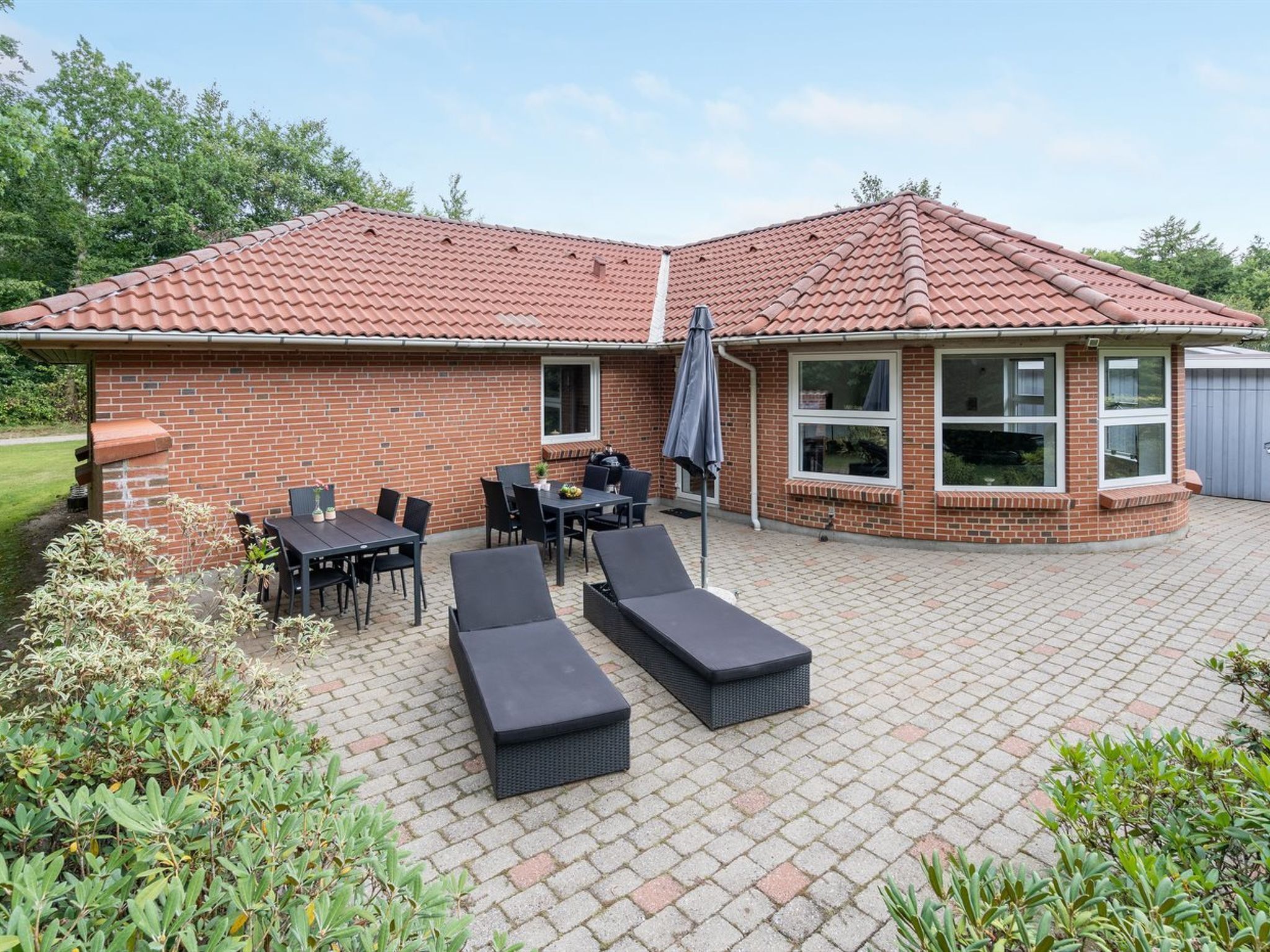 Une maison en briques avec un toit en tuiles, un espace extérieur aménagé avec des tables et des chaises, et un barbecue.