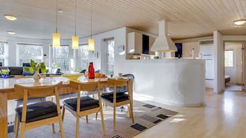 A modern kitchen with wooden cabinets, a central island, pendant lighting, and a view of the living area.