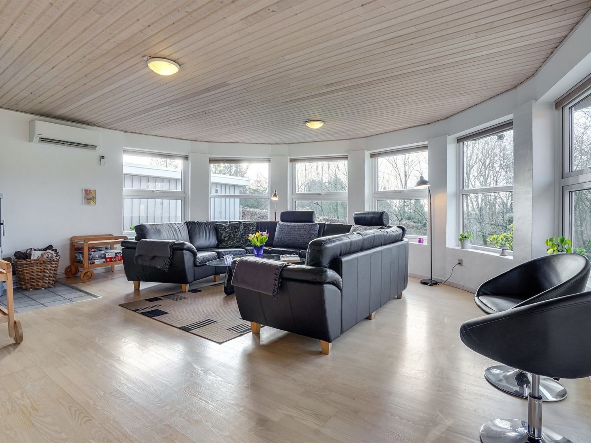 A spacious living room with a curved ceiling, large windows, a black leather sofa, a coffee table, and a modern chair.