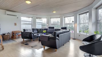 A spacious living room with a curved ceiling, large windows, a black leather sofa, a coffee table, and a modern chair.