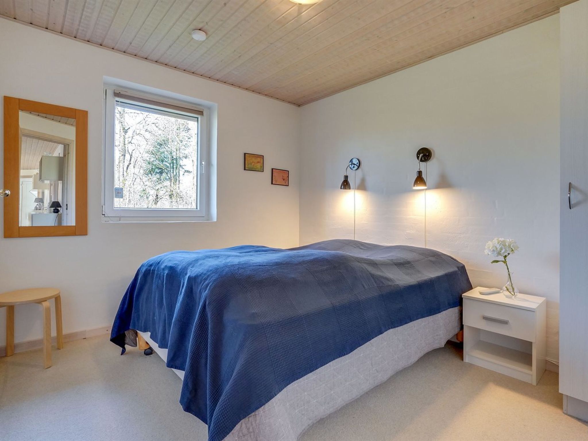 A bedroom with a bed, a window, a bedside table, and a nightstand.