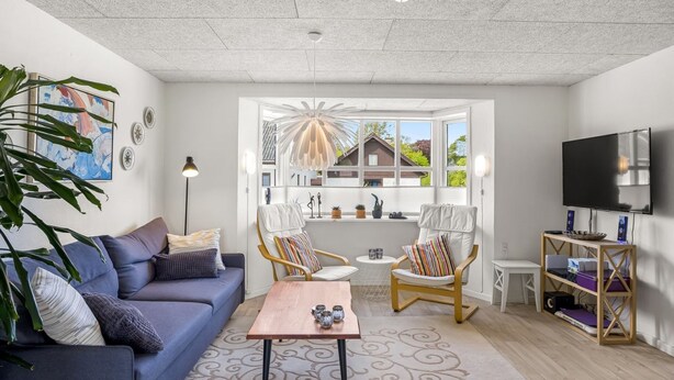 A modern living room with a sofa, chairs, a coffee table, a TV, and a large window with a view of houses.
