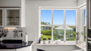 A modern kitchen with a large window, two black chairs, and a greenhouse visible outside.