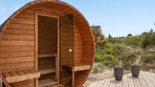 A wooden sauna with a glass door, a wooden deck, and potted plants.