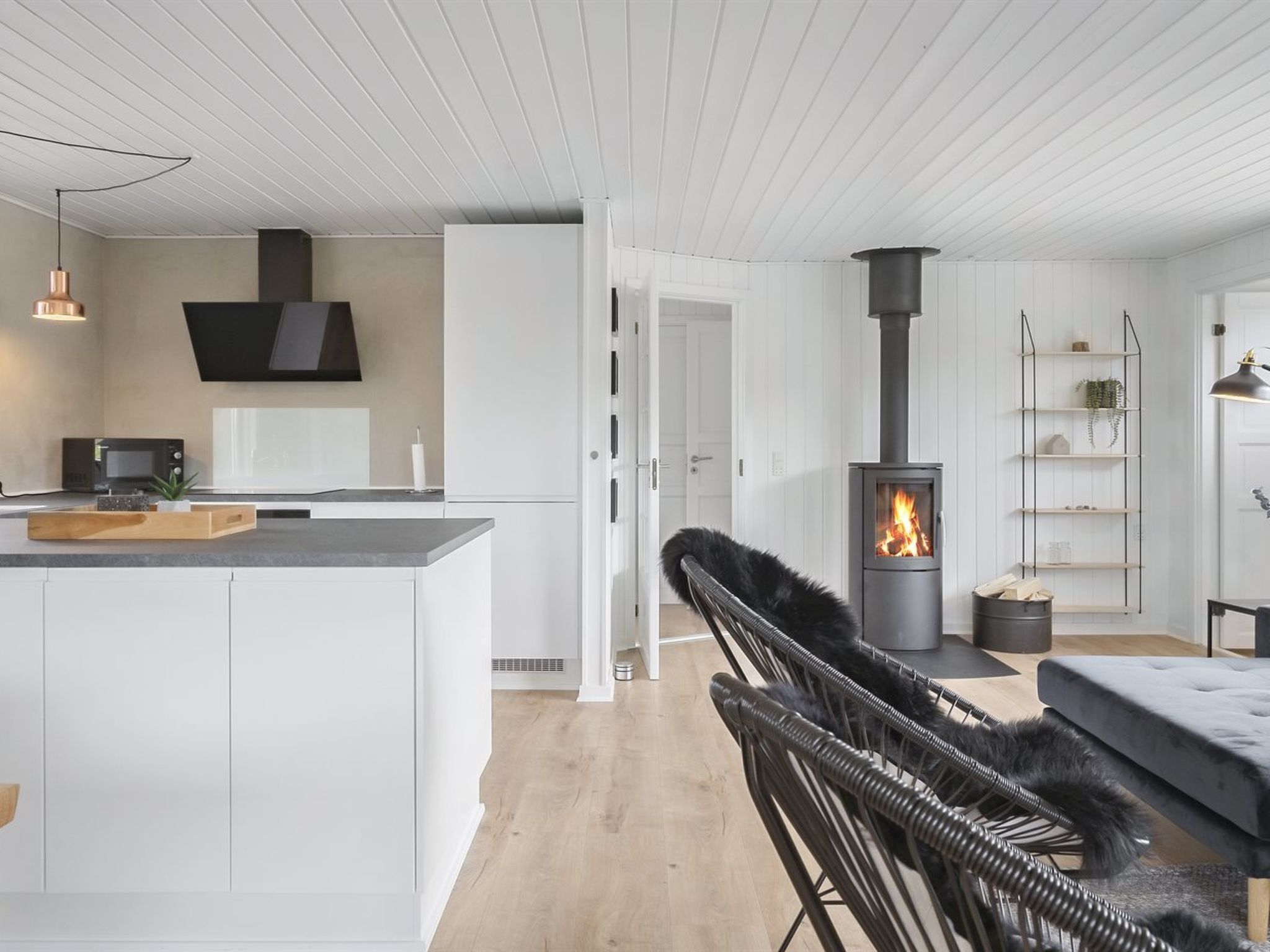 Una cocina moderna con armarios blancos, una isla central, una silla negra y una estufa de leña.