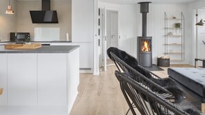 A modern kitchen with white cabinetry, a central island, a black chair, and a wood-burning stove.