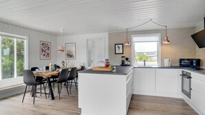 A modern kitchen with white cabinetry, a wooden dining table, black chairs, and pendant lights.